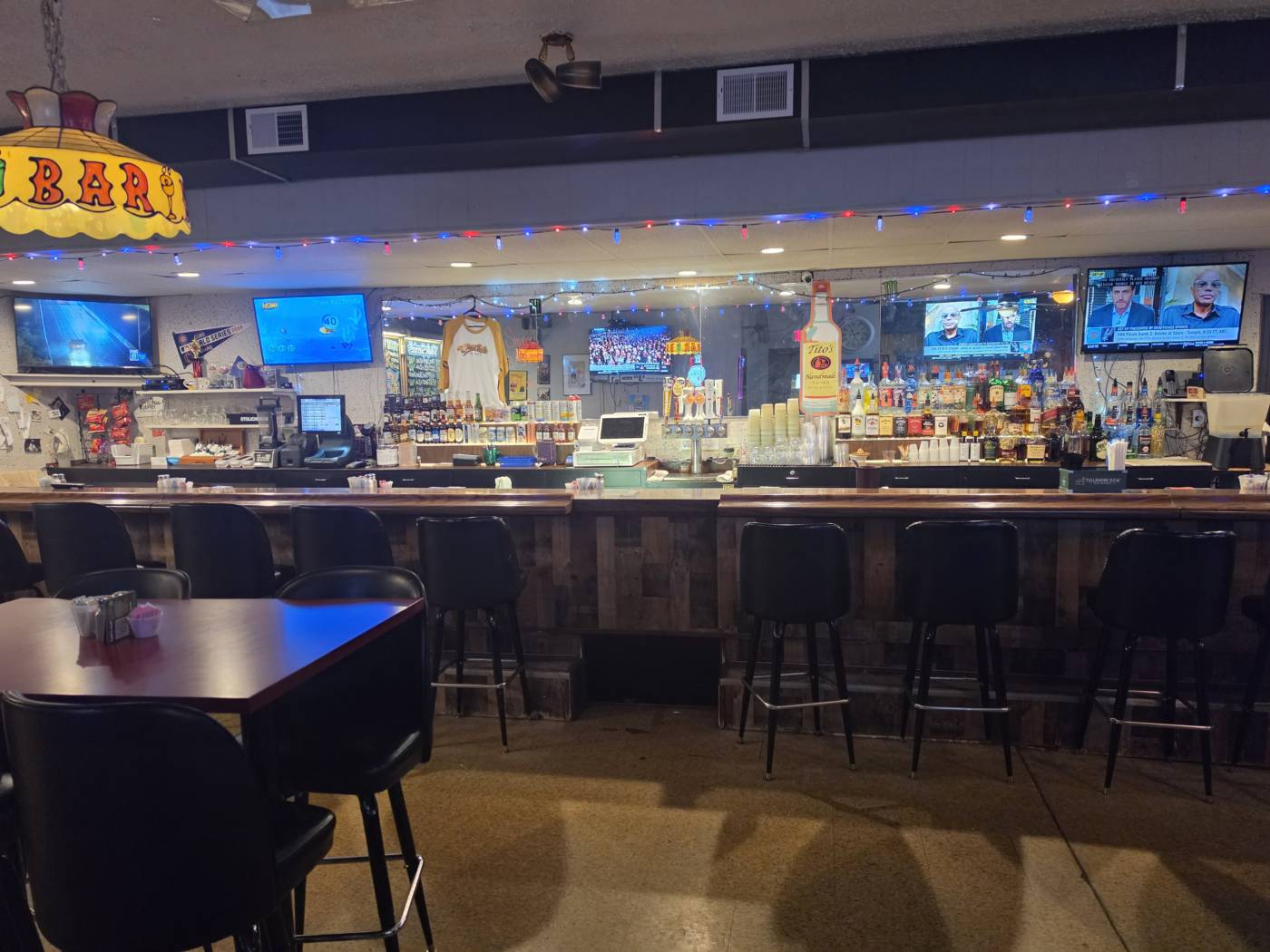 The bar at Houston Pub in daylight — wood-clad counter, taps, backlit bottles and the stained-glass BAR lamp