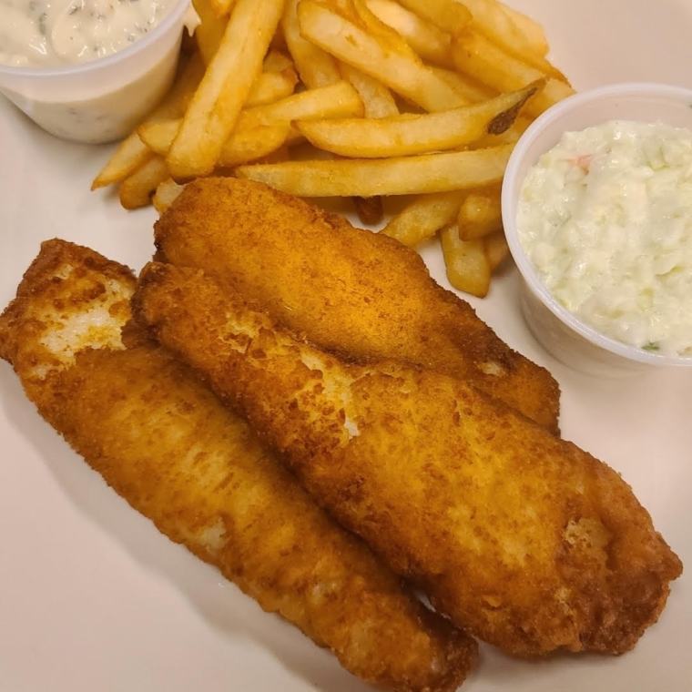 The fried flounder dinner on a white plate — two golden fillets with fries, coleslaw and tartar sauce