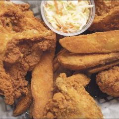 A basket of fried chicken with jojo potato wedges and a cup of coleslaw