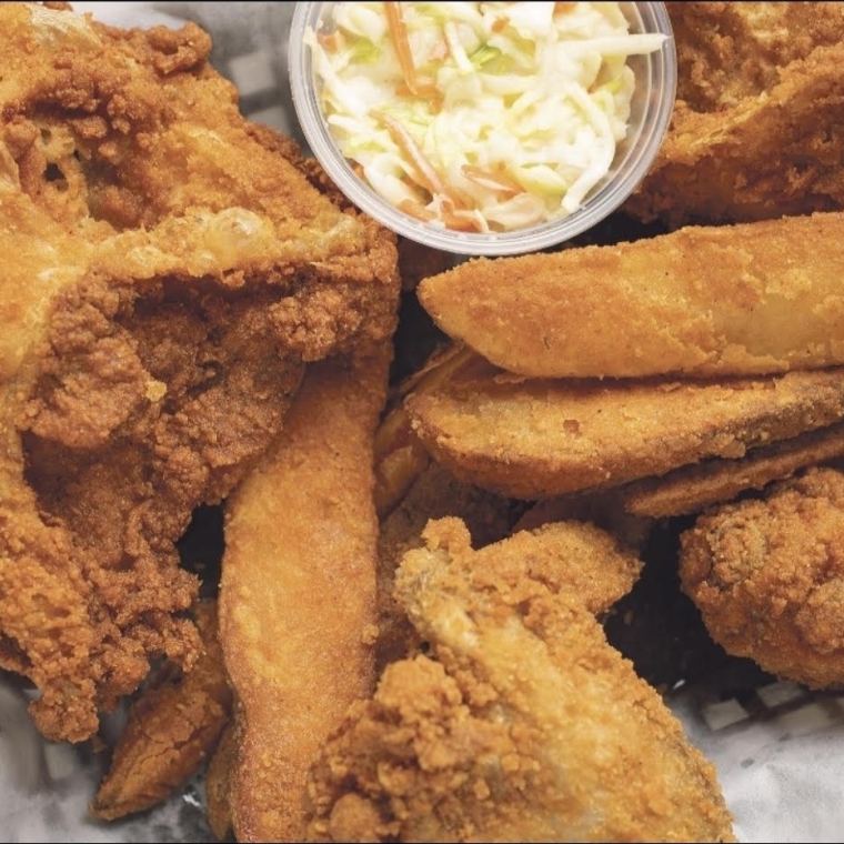 A basket of fried chicken with jojo potato wedges and a cup of coleslaw