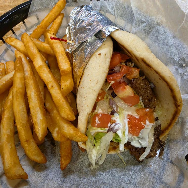 A gyro wrapped in foil — pita, gyro meat, lettuce, tomato, onion and tzatziki — in a paper-lined basket with fries