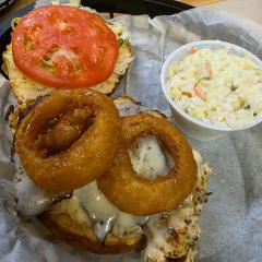 The honey garlic chicken sandwich under melted Swiss and onion rings, with lettuce and tomato on the top bun and a cup of coleslaw alongside