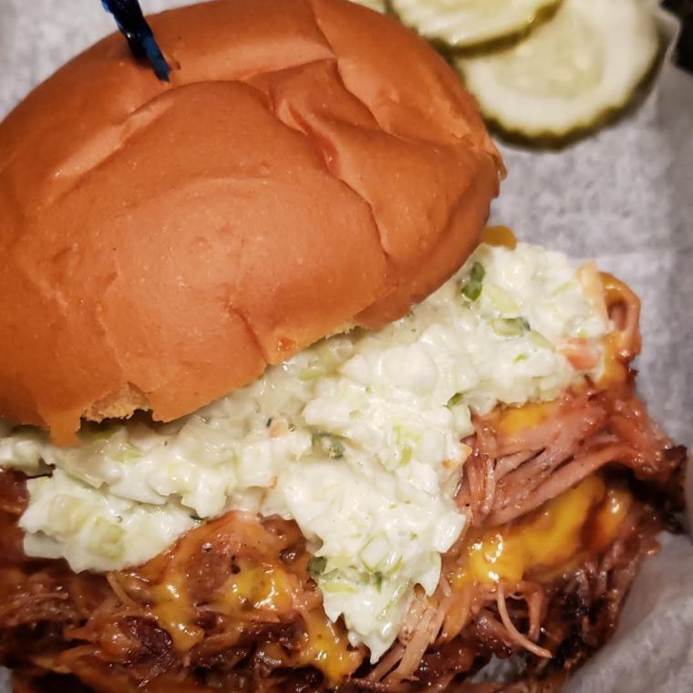 The BBQ pork po'boy — pulled pork and melted cheddar under a pile of coleslaw on a bun, pickle chips alongside