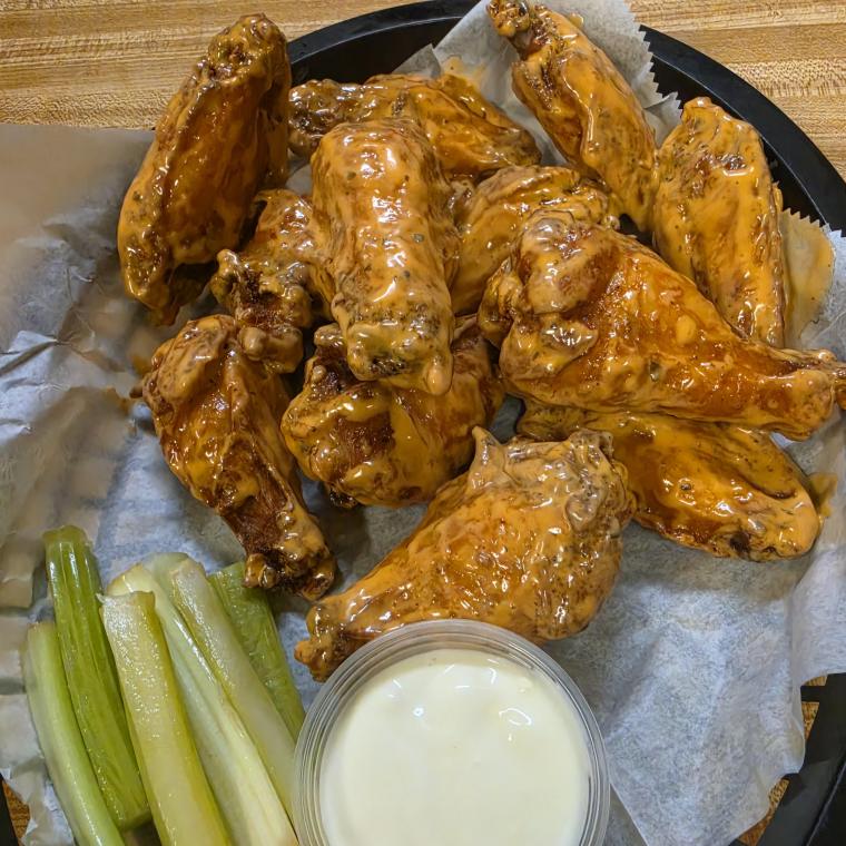 A basket of wings tossed in sauce on the butcher block, with celery sticks and a cup of dressing