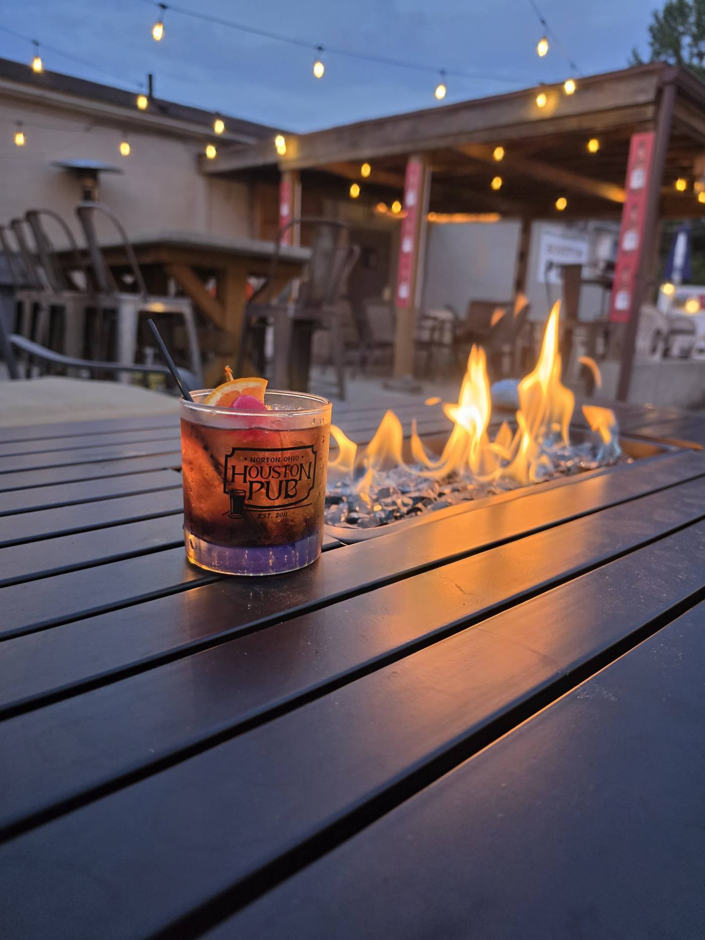 An old fashioned in a Houston Pub rocks glass beside the patio fire table at dusk