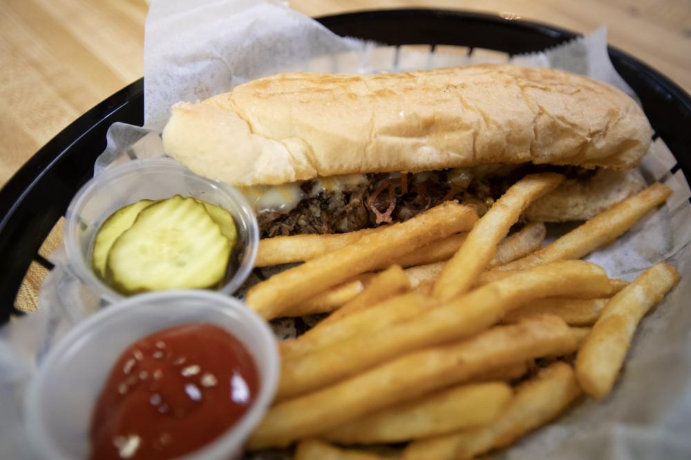 A steak sub in a paper-lined basket with fries, pickle chips and ketchup