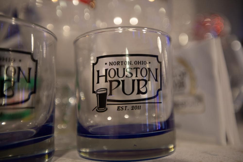 A Houston Pub rocks glass on the bar, the Norton, Ohio badge and EST. 2011 mark facing out under string lights