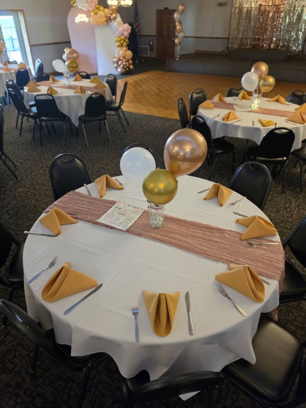 A 60th-birthday table setting — gold napkins, dusty-rose runners and balloons