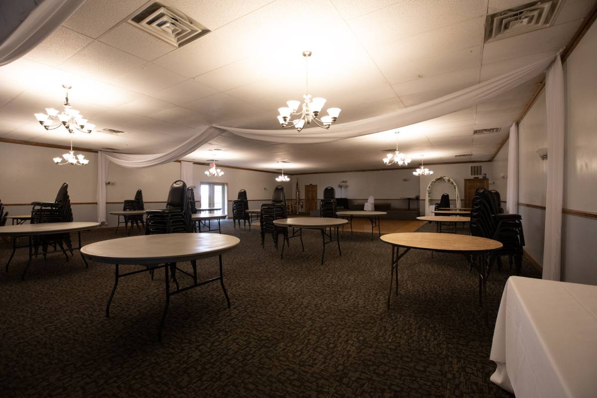 Houston Hall undressed between events — round tables, stacked chairs, ceiling draping, chandeliers and the parquet dance floor