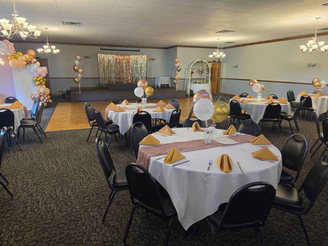 Houston Hall set for a celebration — stage with gold fringe backdrop, parquet dance floor, balloon arch and chandeliers