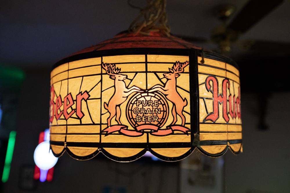 A vintage Hudepohl Pure Grain Beer stained-glass lamp — two stags flanking a barrel — hanging over the bar