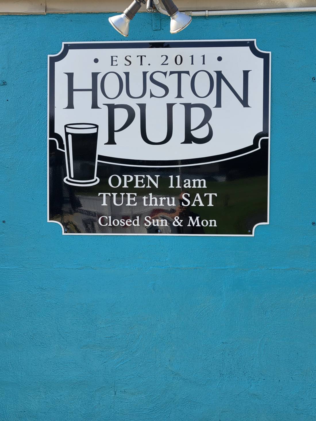The Houston Pub badge sign on the teal wall — EST. 2011, open 11 AM Tue thru Sat, closed Sun and Mon